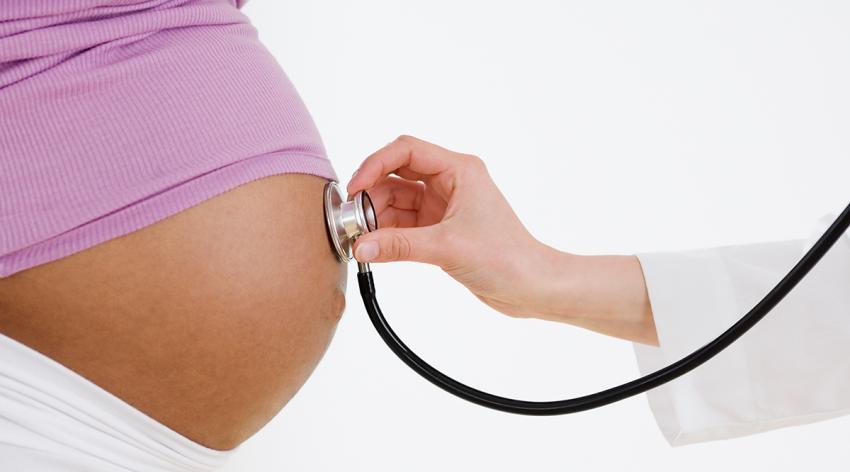 Doctor holding stethoscope on pregnant woman's belly